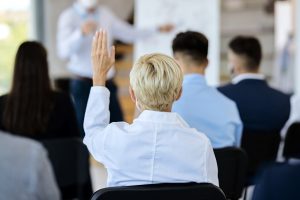 back view of businesswoman attending a seminar and raising her arm to ask a question.